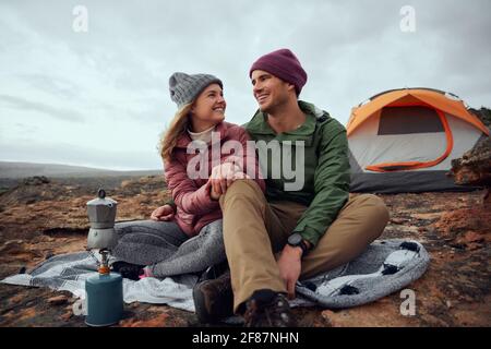 Lächelnder junger Mann und Frau, die sich gegenseitig anblicken Liebe und Vorbereitung Morgengetränk auf dem Campingplatz im Winter Stockfoto