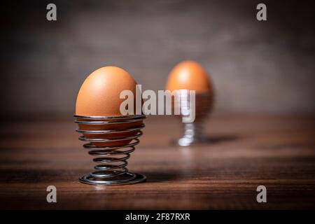 Gekochtes Ei in einem Metall-Spiraleierbecher auf einem Holztisch. Stockfoto