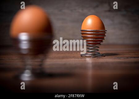 Gekochtes Ei in einem Metall-Spiraleierbecher auf einem Holztisch. Stockfoto