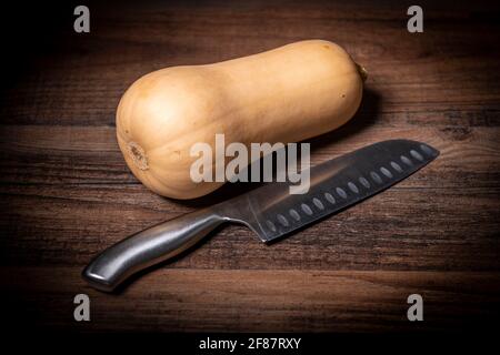Ganze Butternut mit einem Messer auf einer Holzplatte zusammendrücken. Stockfoto