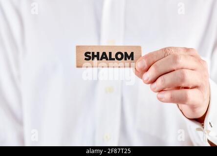 Männliche Hand hält einen Holzblock mit dem Wort Shalom. Begrüßung der Hello-Nachricht. Stockfoto