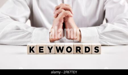 Das Wort Schlüsselwörter auf Holzwürfel mit einem Geschäftsmann mit Spange Hände Hintergrund geschrieben. Suchmaschinenoptimierung und Online-Marketing-Konzept. Stockfoto