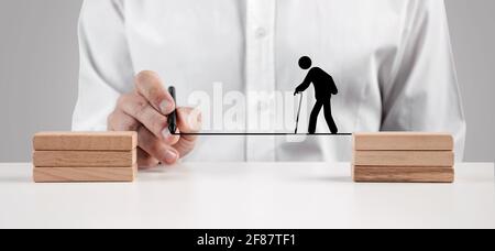 Männliche Hand zeichnet eine Linie zwischen den Holzblöcken für eine ältere Person Ikone mit einem Stock zu gehen. Sicherheit, Unterstützung, Versicherung oder Pflege für Senioren Stockfoto