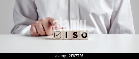 Geschäftsmann drückt mit dem Finger auf die Holzwürfel mit der Abkürzung ISO mit Häkchen. ISO-Qualitätskontrollzertifizierungskonzept. Stockfoto