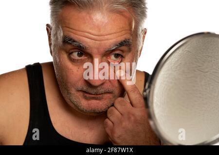 Mann mittleren Alters, der sein unteres Augenlid auf weißem Hintergrund stampft Stockfoto