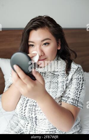 Schöne junge Frau, die auf dem Bett sitzt und ein durchscheinendes Gesicht aufführt Puder beim Make-up Stockfoto