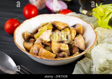 Hähnchenschenkel mit Pilzen, Sellerie, Zwiebeln und Pfeffer eintoben. Hähnchen unter Rühren auf Holzgrund braten Stockfoto