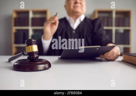 Senior Richter mit Stift und Zwischenablage sitzen am Tisch geschossen Mit Schwerpunkt auf Schläger Stockfoto