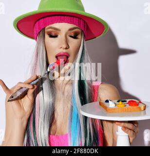 Modische Frau moderne Künstlerin hält Tablett mit Brot mit Ölfarben darauf und essen es mit Spachtel, lecken Stockfoto