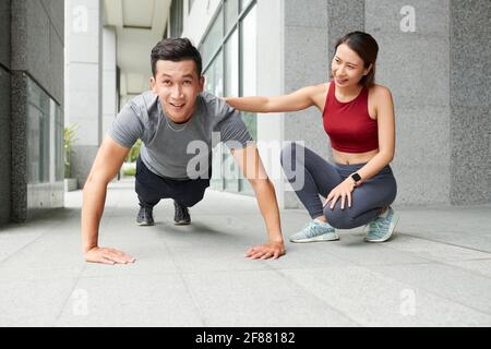 Weibliche Coach Controlling fit jungen Mann tun Liegestütze im Freien Stockfoto
