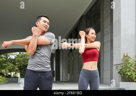 Positives junges asiatisches Paar, das nach dem Joggen im Freien die Arme streckt Stockfoto