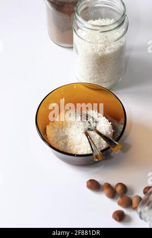 Gesunde Ernährung. Kokosflocken in Schale und Glasglas, Kanne Kakaopulver und Nüsse auf Weiß. Stockfoto