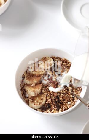 Milch in Müslischale mit Bananenscheiben gießen. Frühstück Vorbereiten. Stockfoto