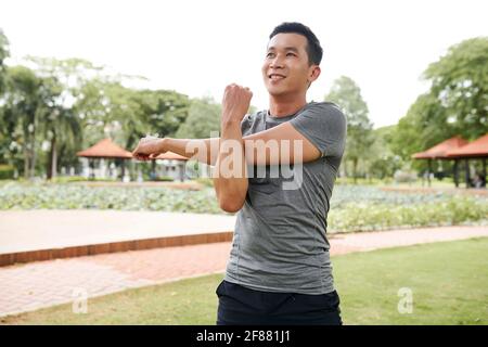 Porträt von gut aussehend fit junge asiatische Mann die Arme und Aufwärmen nach dem Joggen im Freien Stockfoto