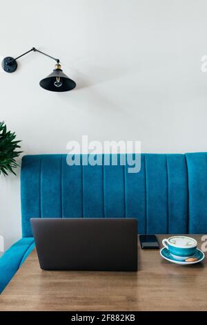 Moderner Laptop mit Telefon und einer Tasse Matcha-Kaffee in einer großen Tasse auf dem Tisch. Stilvolles Café für freiberufliche Arbeit. Speicherplatz kopieren Stockfoto