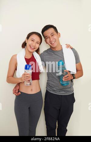 Portrait von glücklichen jungen asiatischen Paar mit Handtuch und frisch Wasserflaschen umarmen und lächeln die Kamera an Stockfoto