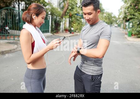 Junges asiatisches Paar, das Anwendungen auf Smartphone und Smart Watch setzt Vor dem Training im Freien Stockfoto