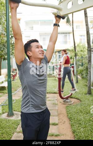 Gut aussehend fit junge asiatische Mann macht Übungen auf Fitnessgeräten Im Stadtpark Stockfoto