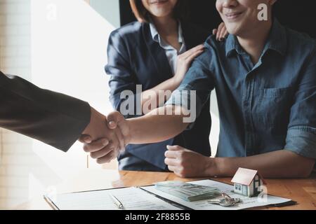 Junges asiatisches Paar, das nach Vertragsunterzeichnung mit Immobilienmakler die Hände schüttelt. Immobilienkonzept. Stockfoto