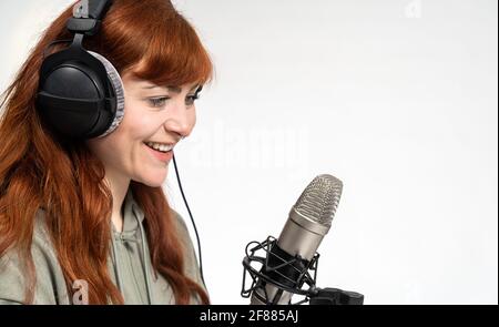 Porträt eines Mädchens mit roten Haaren vor weißem Hintergrund Sprechen in ein Sendemikrofon Stockfoto