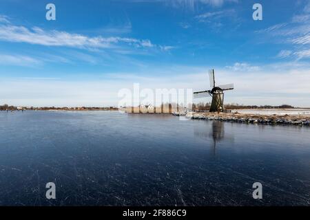 Winterlandschaft mit Eis auf dem Dieperpoel (Kagerplassen) vor einer Windmühle (de Kok) und Haus auf dem Kogjespolder in den Niederlanden. Stockfoto