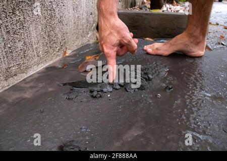 St. James, Barbados - 11 2021. April: Weißer Mann zieht den Finger durch die nasse Vulkanasche des Soufriere-Vulkanausbruchs von St. Vincent. Schwerer Ascheabfall. Stockfoto