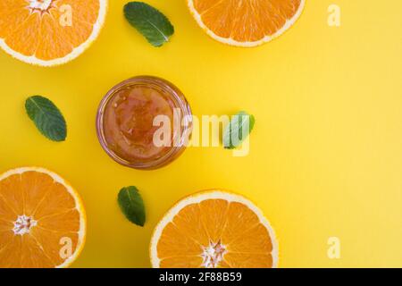 Hausgemachte Orangenmarmelade im Glas und Orangenhälften auf dem gelben Hintergrund.Draufsicht.Platz kopieren. Stockfoto