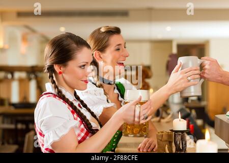 Zwei junge Frauen, die in traditionelle bayerische Tracht sitzen im Restaurant oder im Pub mit Bier Stockfoto