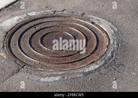 Runde Kanalschachtluke ist in städtischen Asphaltstraße Stockfoto