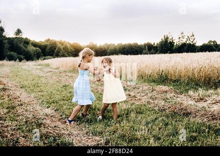 Familienleben und Sommerkonzept. Zwei emotionale Schwestern tanzen bei Sonnenuntergang mit Roggen auf dem Feld. Stockfoto