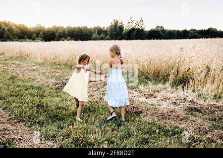 Zwei emotionale Schwestern tanzen bei Sonnenuntergang mit Roggen auf dem Feld. Lifestyle- und Sommerkonzept Stockfoto