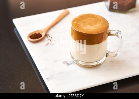 Dalgona Kaffee, flauschiger cremiger Shake-Kaffee in einem transparenten Glas auf einem Marmorboden neben einem Holzlöffel. Sehr beliebt in Korea. Stockfoto