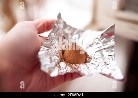 Eine weibliche Hand hält eine Schokolade Trüffel Süßigkeiten eingewickelt Eine Folienverpackung Stockfoto