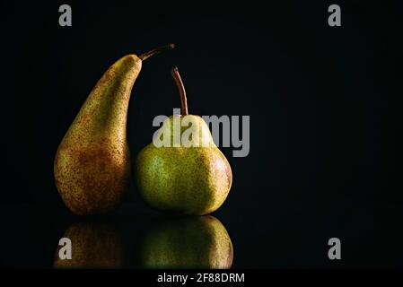 Zwei Birnen verschiedener Sorten auf schwarzem matten Hintergrund. Das Konzept von Toleranz und Körperpositiver. Stockfoto