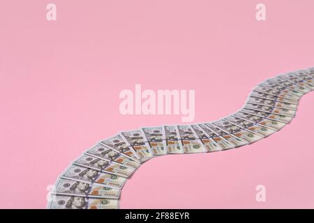 Geldweg aus 100-Dollar-Scheinen auf rosa Hintergrund mit Kopieplatz. Stockfoto