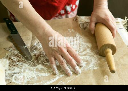 Mamas Kuchen. Weibliche Hände bereiten den Teig mit einem Nudelholz für den Kuchen vor. Kochen während der Quarantäne. Stockfoto