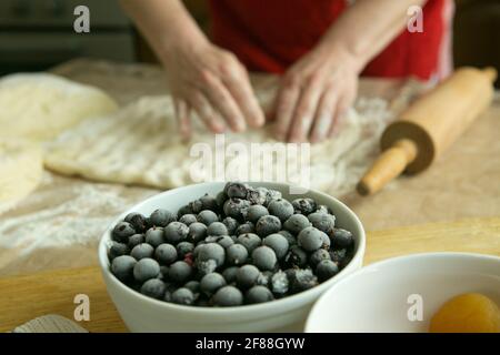Mamas Kuchen. Füllung für Obstkuchen: Gefrorene schwarze Johannisbeere. Vor dem Hintergrund der Hände meiner Mutter bereiten sie den Teig für den Kuchen vor. Garzeit Stockfoto