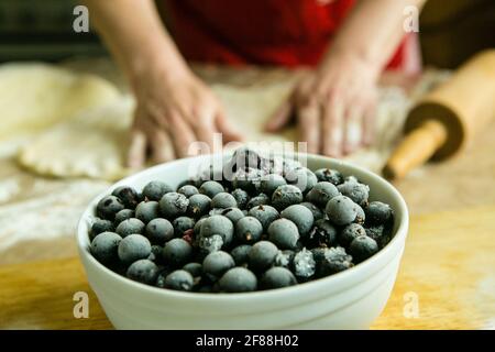 Mamas Kuchen. Füllung für Obstkuchen: Gefrorene schwarze Johannisbeere. Vor dem Hintergrund der Hände meiner Mutter bereiten sie den Teig für den Kuchen vor. Garzeit Stockfoto