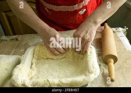 Mamas Kuchen. Weibliche Hände geben den Teig in die Form. Kochen während der Quarantäne. Stockfoto