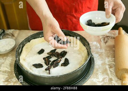 Mamas Kuchen. Der Teig wird in eine Backform gegeben. Die erste Schicht der Füllung sind genähte Pflaumen. Kochen während der Quarantäne. Stockfoto