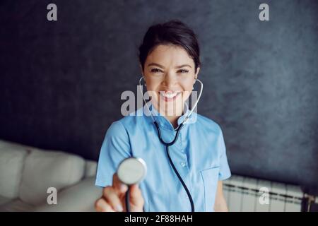 Lächelnde Ärztin, die das Stethoskop in die Kamera hält, als ob sie die Lungen untersucht. Selektiver Fokus auf den Arzt. Stockfoto