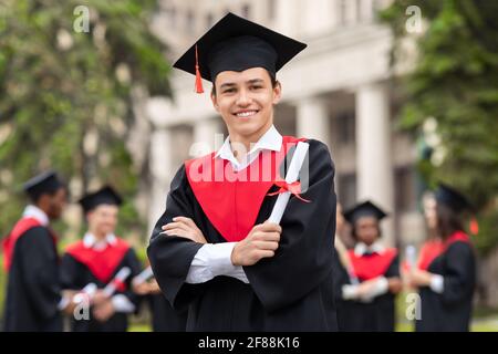 Fröhlicher Kerl im Abschlusskostüm mit Diplom Stockfoto