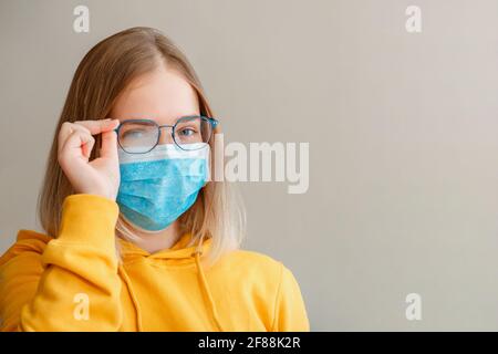 Neblige Brille trägt auf junge Frau. Teenager-Mädchen in blauen medizinischen Schutz Gesichtsmaske und Brillen wischt verschwommen neblig vernebelte Gläser mit Kopie s Stockfoto