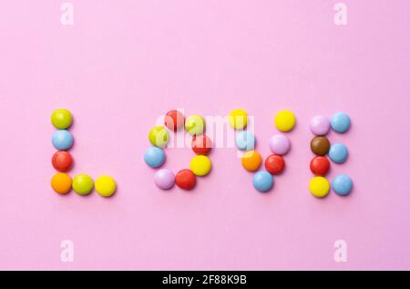 Das Wort LIEBE aus bunten Schokolade Süßigkeiten Smarties auf rosa Hintergrund gemacht.Multicolored Liebe Lebensmittel Hintergrund. Stockfoto