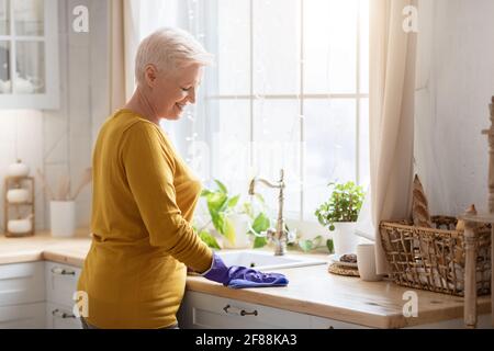 Fröhliche ältere Dame, die die Küche putzt und Gummihandschuhe trägt Stockfoto