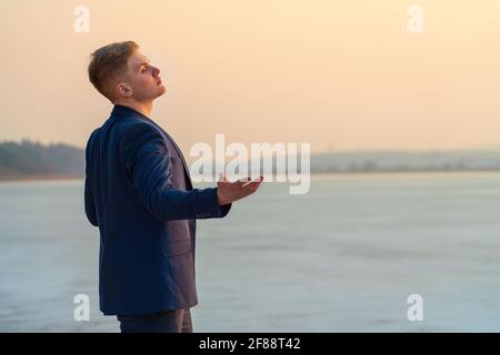 Ein junger Mann drückt Emotionen aus, am Meer, singt und Gesten. Vor dem Hintergrund des Sonnenuntergangs Meer. Stockfoto