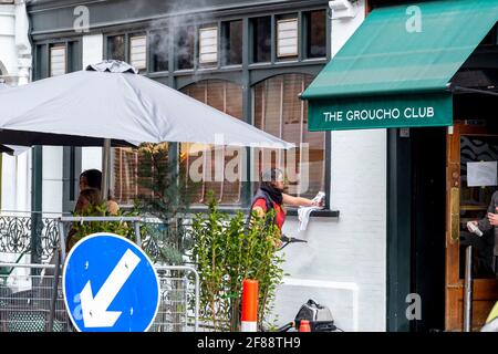 London, Großbritannien. April 2021. Ein Mitarbeiter des Groucho Club in Soho im Zentrum von London putzt, bevor er seine Gäste begrüßt, da die 4. Sperre in Großbritannien gelockert wird, was bedeutet, dass Kunden Getränke und Speisen im Freien bestellen können. Kredit: SOPA Images Limited/Alamy Live Nachrichten Stockfoto