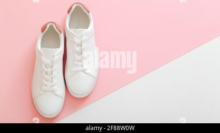 Weiße Sneakers, weibliche weiße Lederschuhe mit Schnürsenkeln auf rosa Hintergrund. Paar stilvolle Sneaker bequeme Sportswear Hipster Damenschuhe. Oben vi Stockfoto