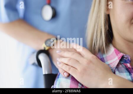 Krankenschwester, die ihre Hand auf die Schulter einer jungen behinderten Frau legt In Nahaufnahme des Rollstuhls Stockfoto