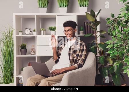 Fotoporträt eines Freiberuflers, der im Stuhl sitzt und Hand in Hand winkt Kamera bei Webmeeting, die von zu Hause aus auf einem Laptop arbeitet Stockfoto